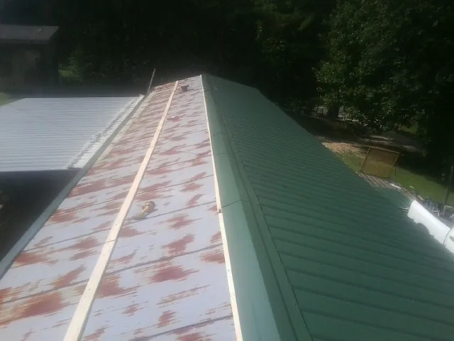 Old rusted panels beside newly installed green metal roofing — Wind Damage Roof Repair by Roofing Brothers in West Point